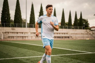 Jeune joueur de football en entraînement au centre de formation de l'Olympique de Marseille, portant une tenue blanche et bleue sur un terrain soigné