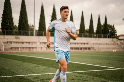 Jeune joueur de football en entraînement au centre de formation de l'Olympique de Marseille, portant une tenue blanche et bleue sur un terrain soigné